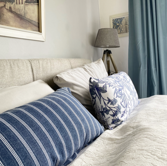 Bett mit blauen Kissen, Schreibtischlampe und türkisfarbenen Vorhängen.