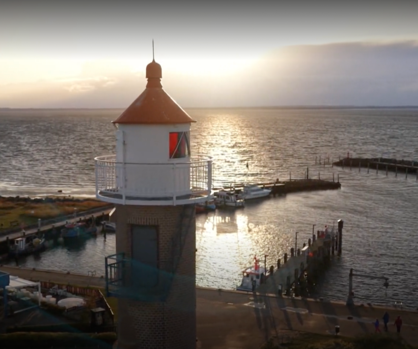 Ein Leuchtturm am Wasser bei Sonnenuntergang mit Booten im Hafen.