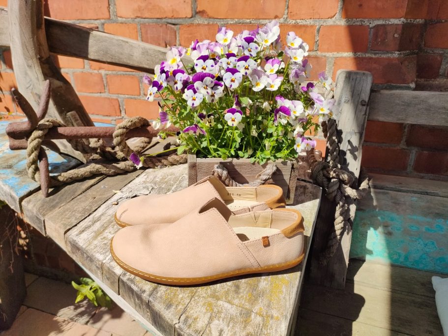 Pflegeleichte Schuhe liegen auf einer Bank neben einem Blumentopf mit bunten Blumen.