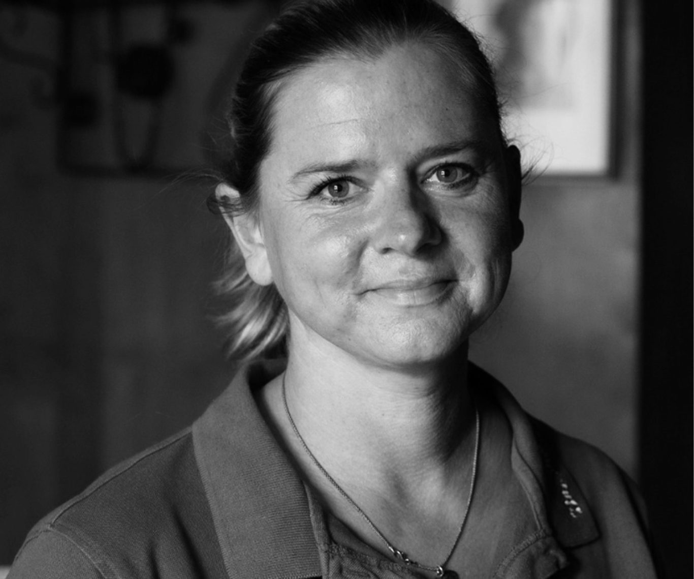 Porträt einer lächelnden Frau mit kurzer, heller Haarfrisur in einem dunklen Umfeld.