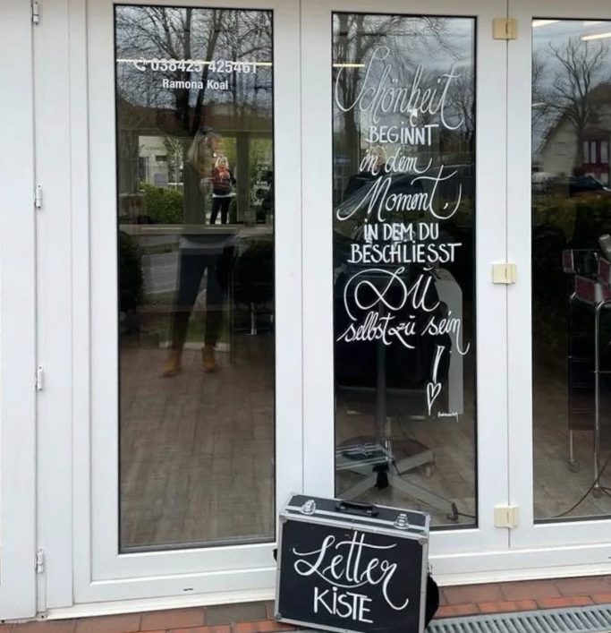 Zwei Glastüren mit geschwungener Schrift und einer Kiste für Briefe davor.