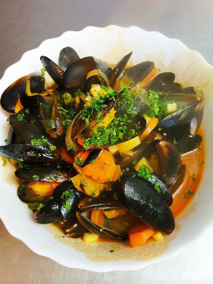 Schüssel mit Muscheln, buntem Gemüse und frischen Kräutern.