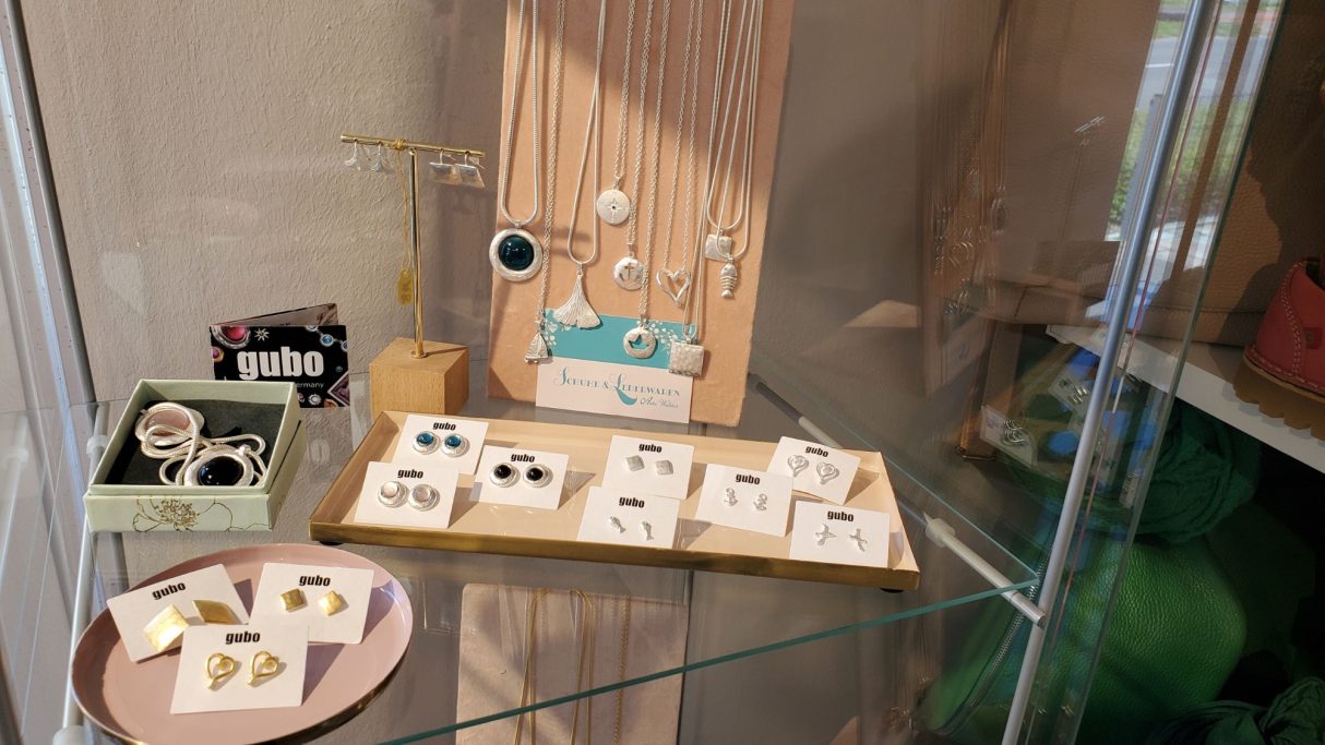 Schmuckauslage mit Ohrringen und Ringen auf einem Holzgestell und in Kästchen.