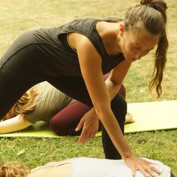 Eine Yoga-Lehrerin unterstützt Teilnehmerinnen bei einer Übung im Freien.