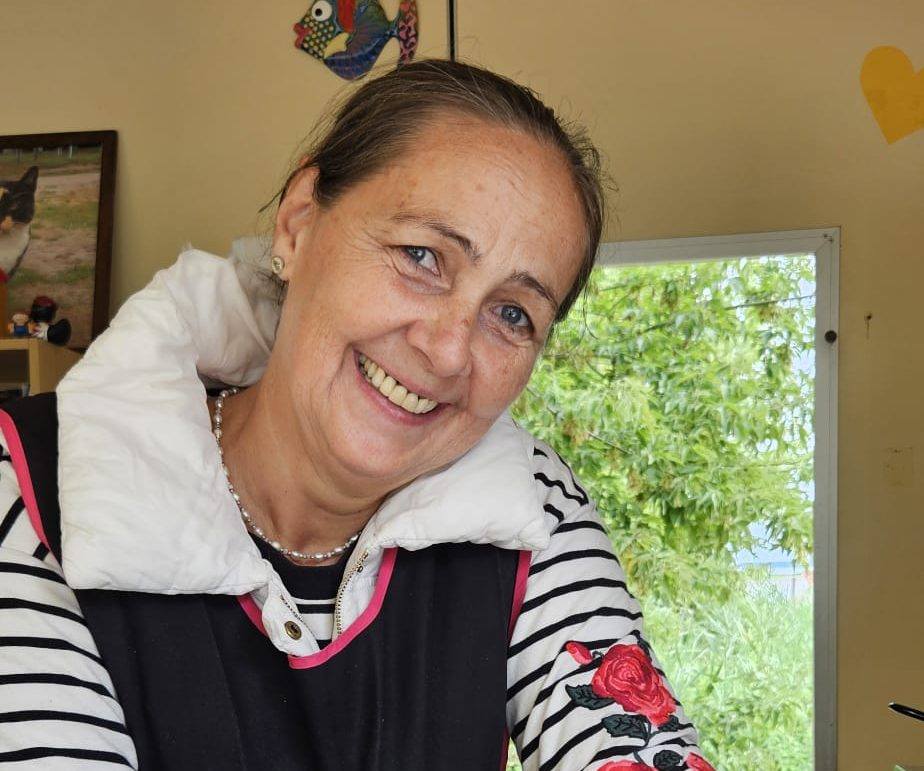 Lächelnde Frau mit gestreiftem Shirt und kragen, vor einem Fenster mit Grün im Hintergrund.