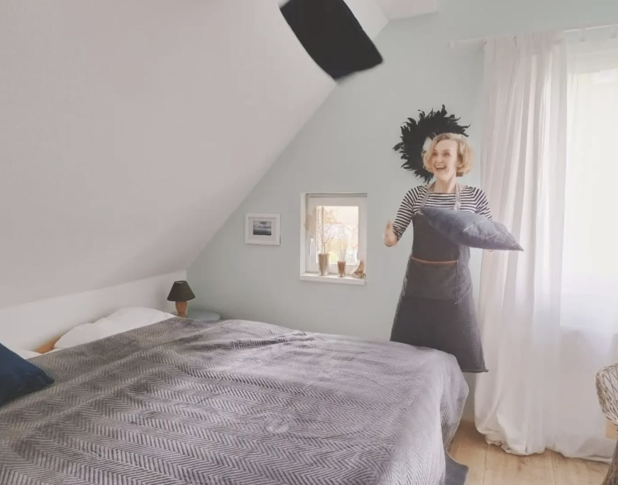Frau mit Kissen in einem hellen, minimalistisch eingerichteten Schlafzimmer.
