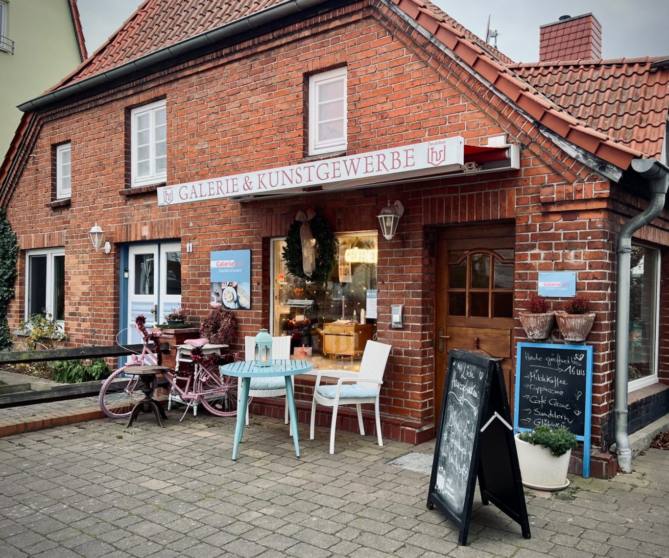 Kleines Café mit roten Markisen, Tischen im Freien und Fahrrädern im Hintergrund.