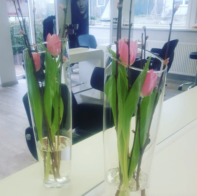 Zwei Vasen mit pinken Tulpen und grünen Blättern auf einem Tisch.