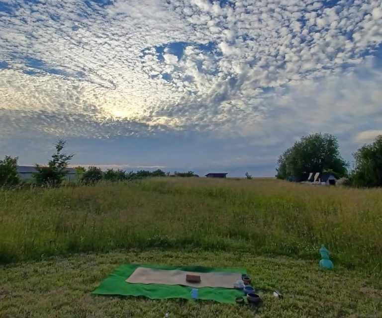 Landschaft mit grünem Gras, Picknickdecke und Himmel voller Wolken bei Sonnenuntergang.