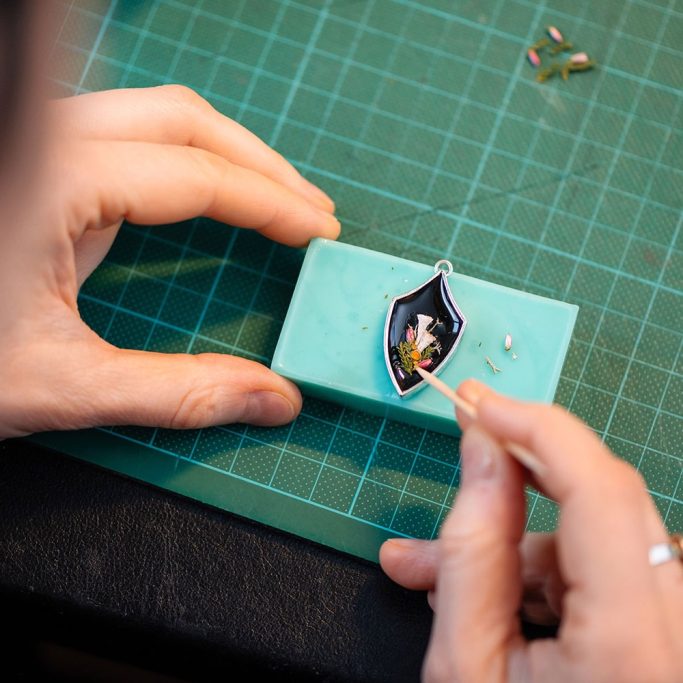 Hände arbeiten an einem kleinen, detaillierten Modell auf einem grünen Schneidebrett.