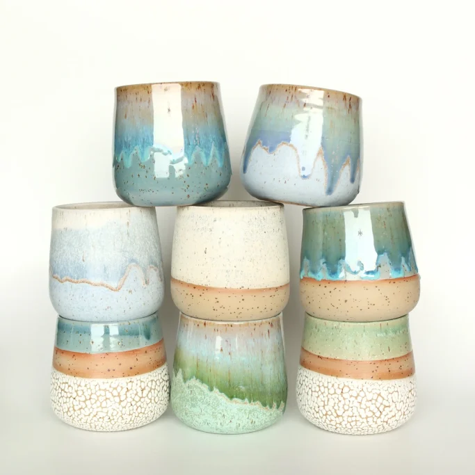 Bunte, handgefertigte Keramiktassen in verschiedenen Formen und Farben gestapelt.