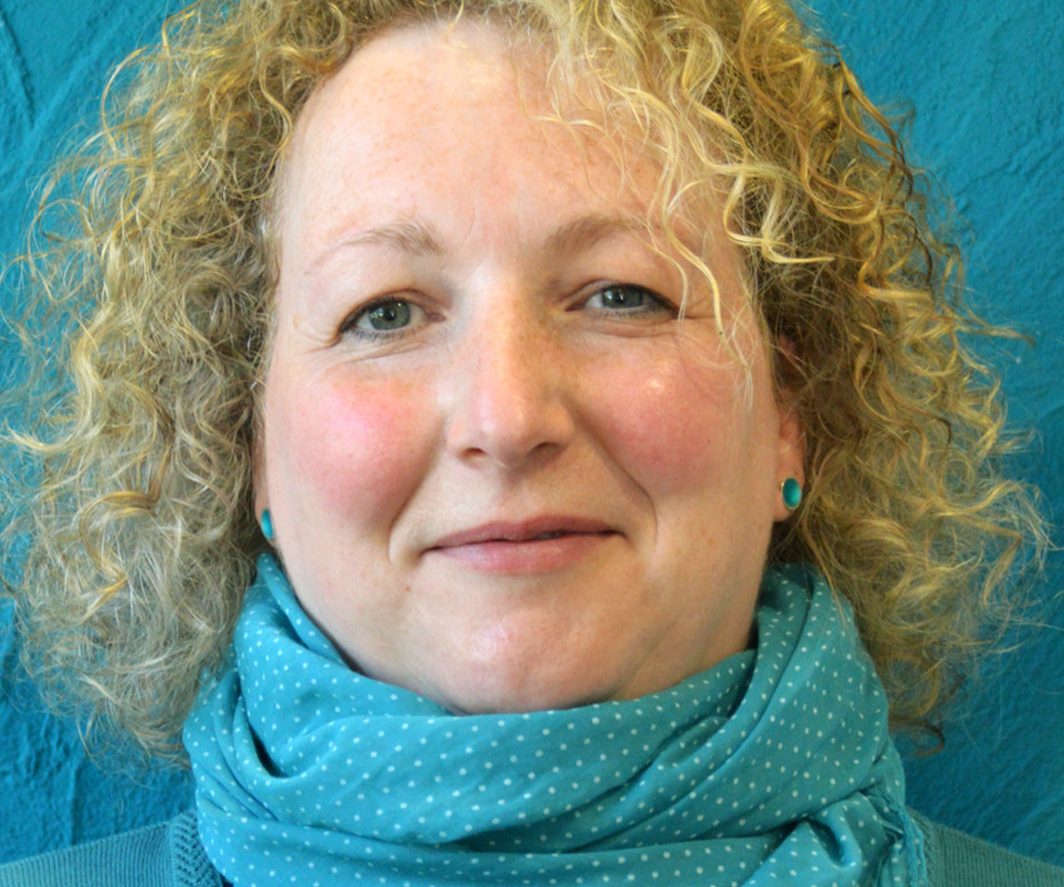 Frau mit lockigem, blonden Haar und türkisem Schal vor blauem Hintergrund.