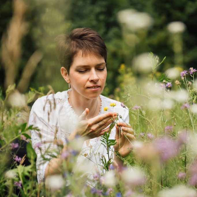 Eine Frau betrachtet eine Blume in einer blühenden Wiese.