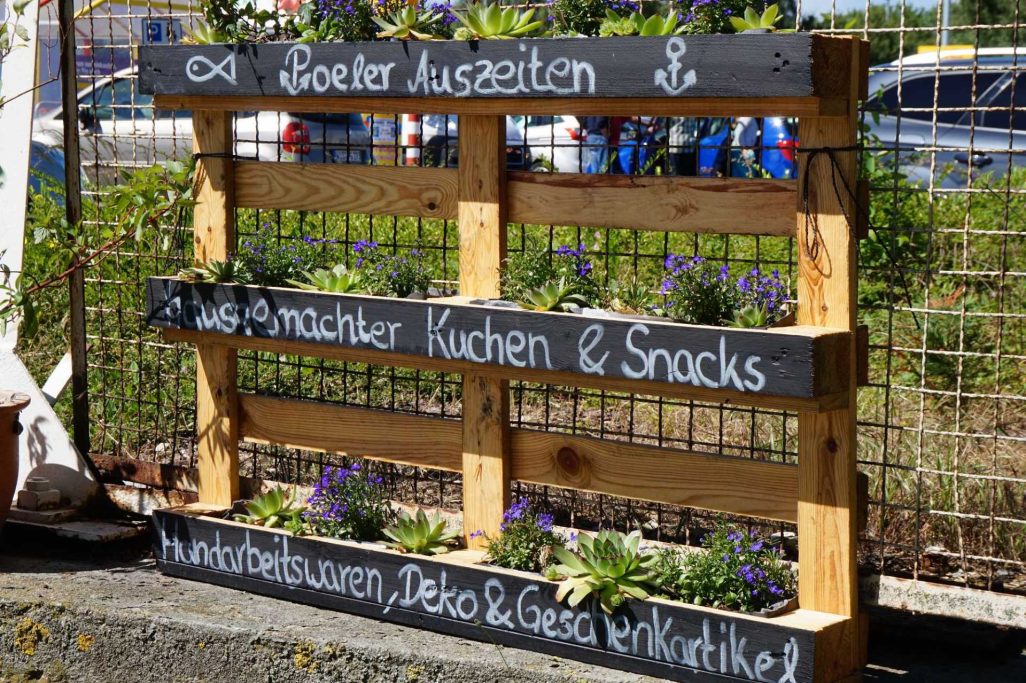 Holzregal mit schwarzer Tafel beschriftet für Speisen und Snacks am Wasser.