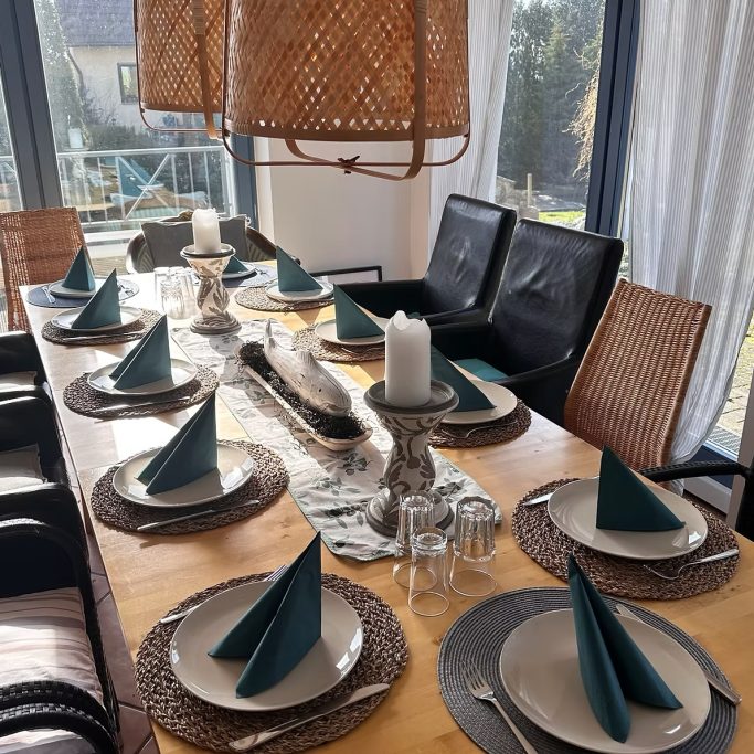 Gedeckter Esstisch mit Kerzen, Servietten und Blick nach draußen.