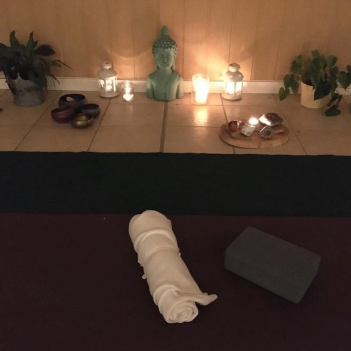 Ein Meditationsbereich mit einer Statue, Kerzen, Pflanzen und einer Yogamatte.