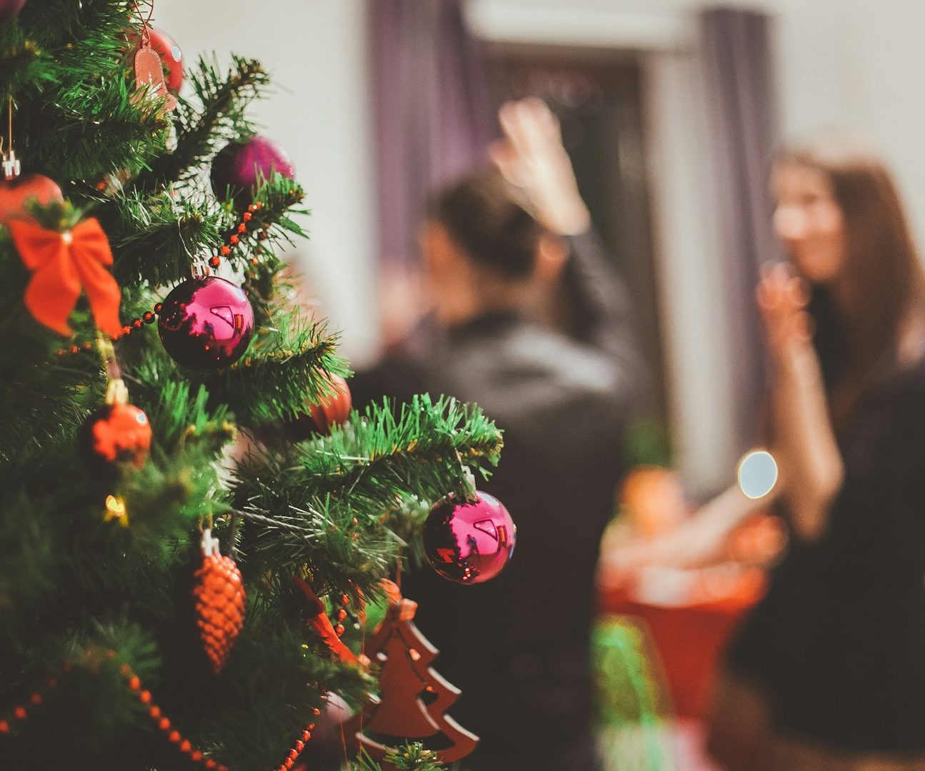 Weihnachtsbaum im Vordergrund, festliche Feier im Hintergrund mit Menschen.
