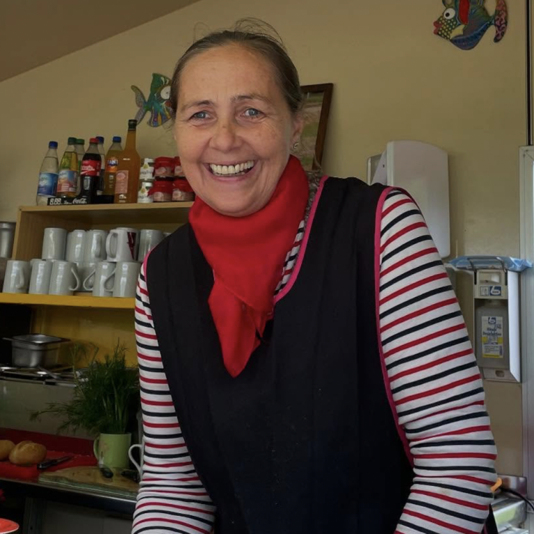 Lächelnde Frau mit rotem Schal und gestreiftem Shirt in einer Café-Küche.