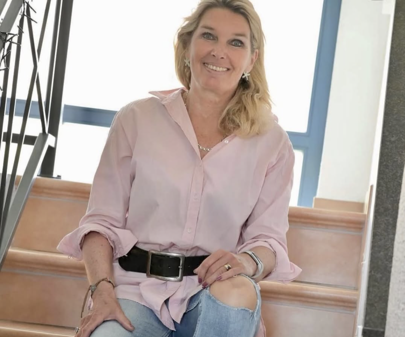 Frau mit blonder Haarfarbe in rosa Bluse sitzt auf Treppe.