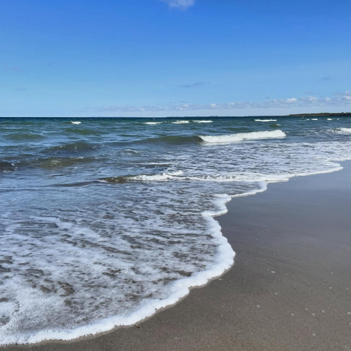 Ruhiger Strand mit sanften Wellen unter einem klaren blauen Himmel.