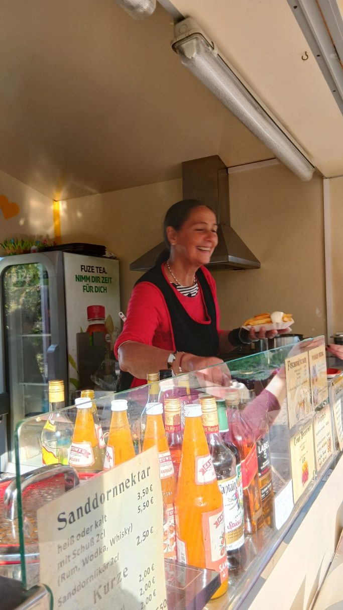 Kiosk mit einer Frau, die Snacks und Getränke verkauft, im Hintergrund Flaschen.