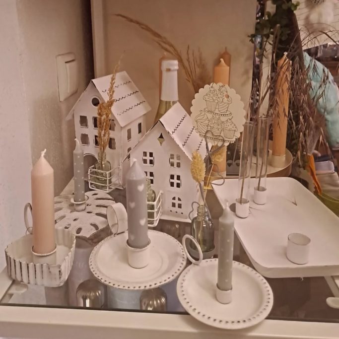 Dekorative Kerzenständer, kleine Häuser und botanische Elemente auf einem Tisch.