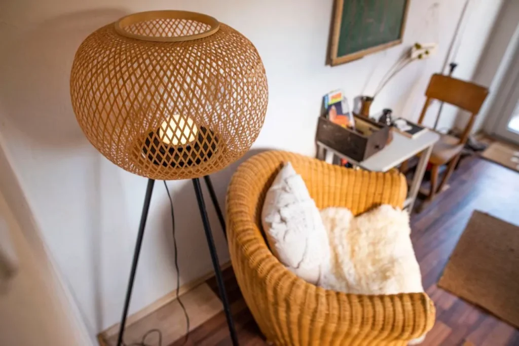Runder Korblampenständer neben einem gemütlichen geflochtenen Sessel.