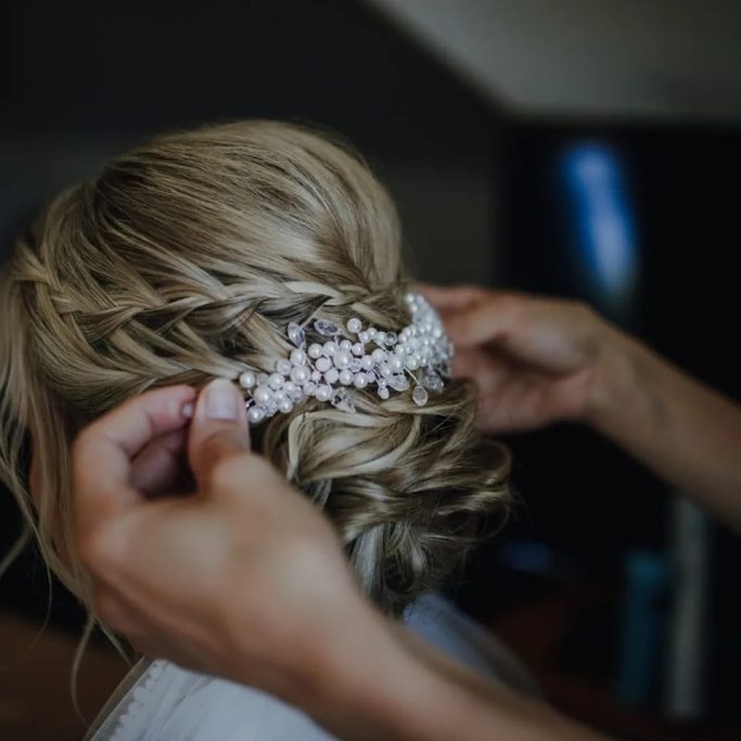 Hochsteckfrisur mit Haarschmuck, Hände zeigen den letzten Schliff.