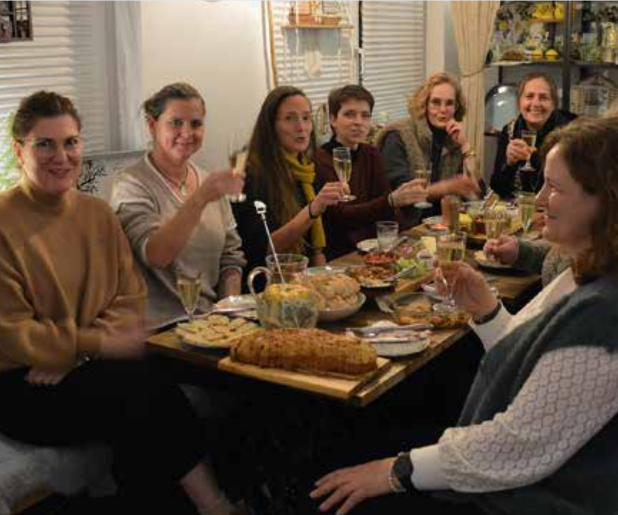 Gruppe von Frauen, die an einem Tisch mit Essen und Getränken feiern.