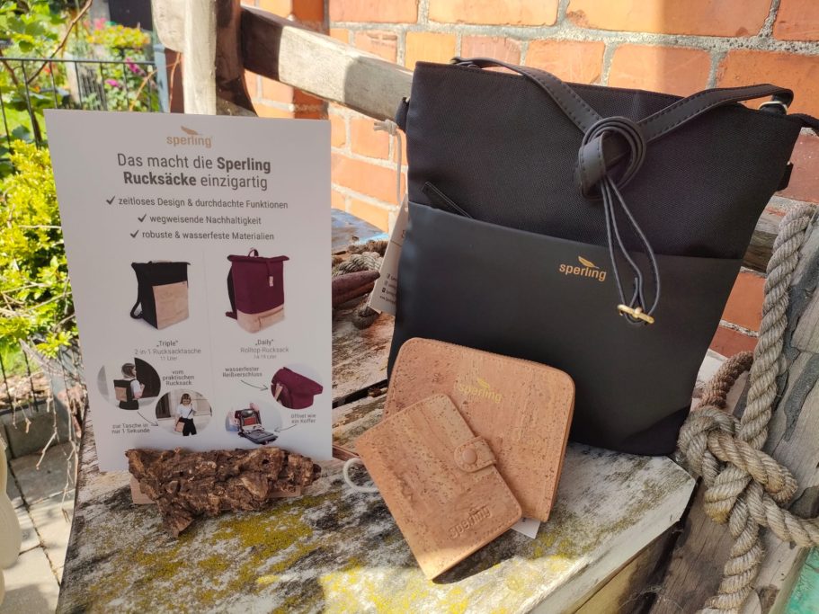 Schwarze Umhängetasche mit Werbeaufschrift und Untersetzer auf einer Bank.