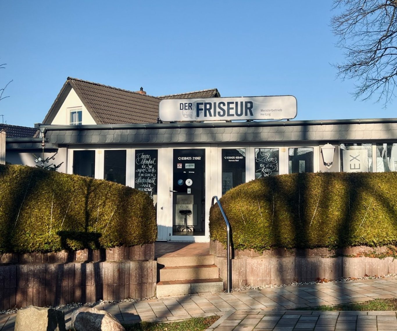 Friseursalon mit begrünter Umgebung und klarer Beschilderung an der Fassade.