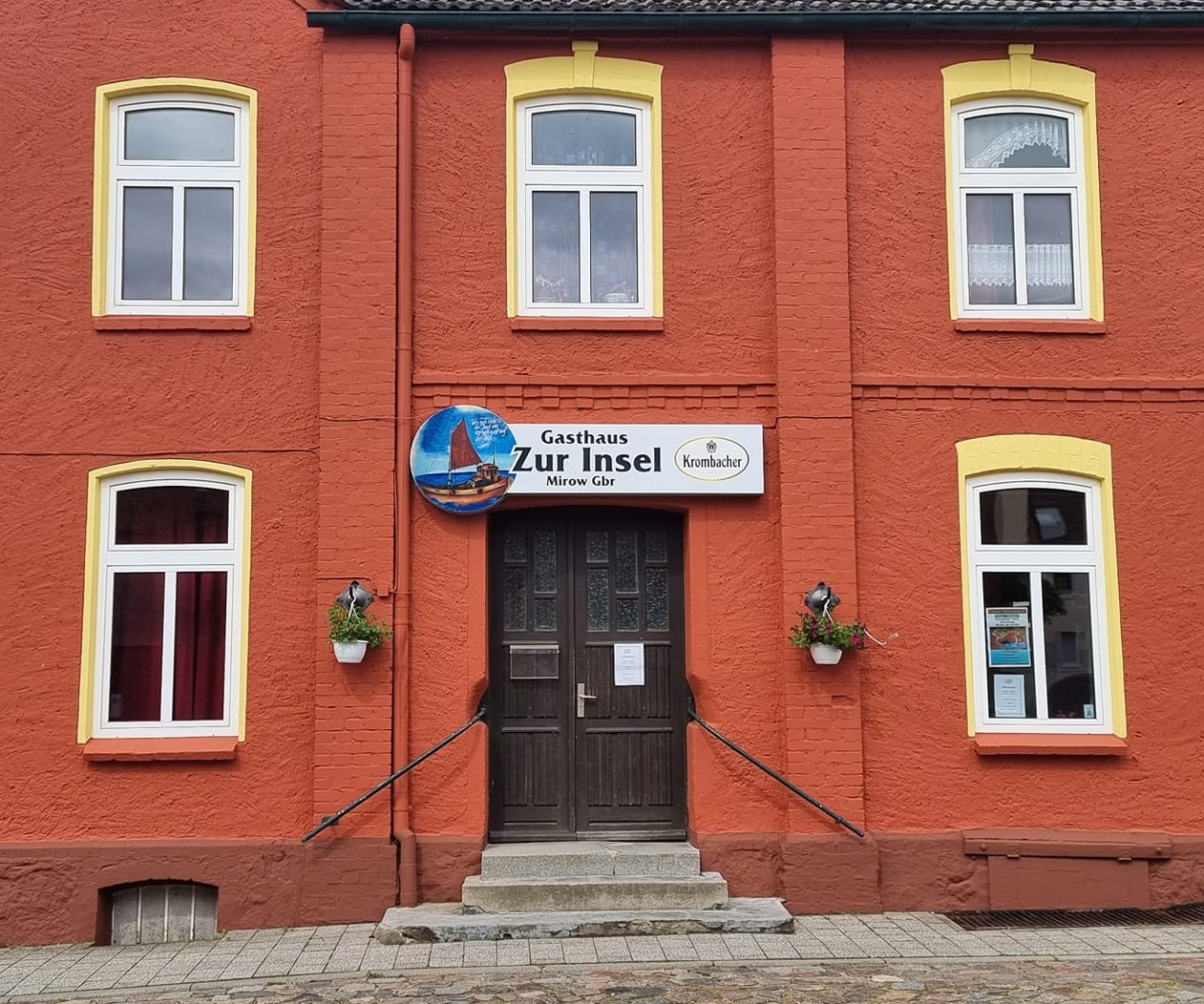 Rotes Gebäude mit mehreren Fenstern und einem Eingang, beschriftet mit "Zur Insel".