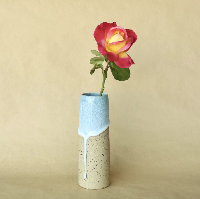 Eine Vase mit einer rot-gelben Rose auf einem beige Hintergrund.