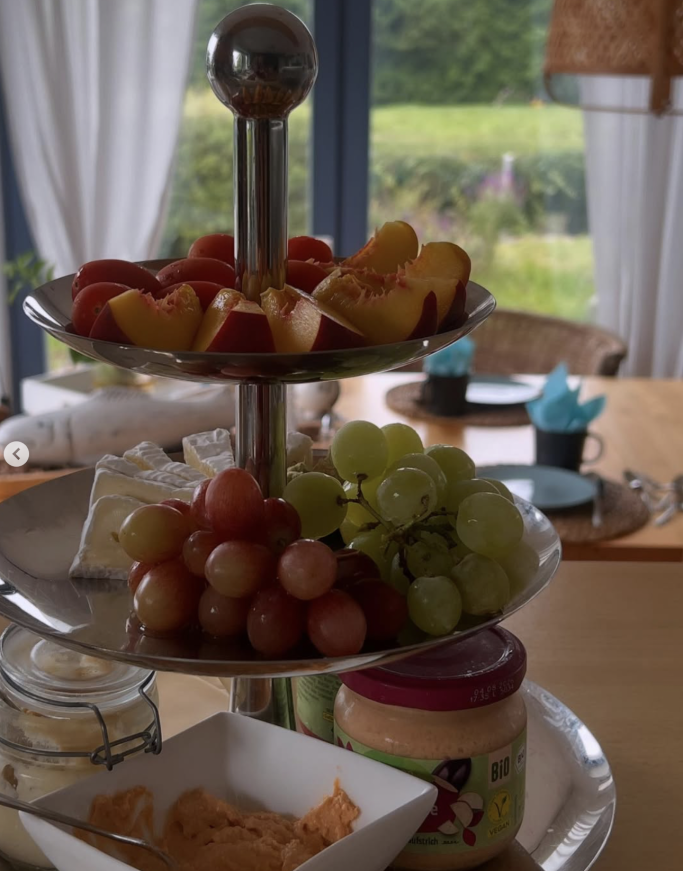 Mehrstöckiger Obstständer mit Äpfeln, Trauben und einer kleinen Schüssel mit Snacks.