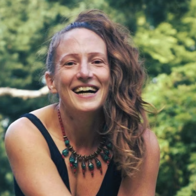 Lächelnde Frau mit lockigem Haar und Halsschmuck, umgeben von Natur.