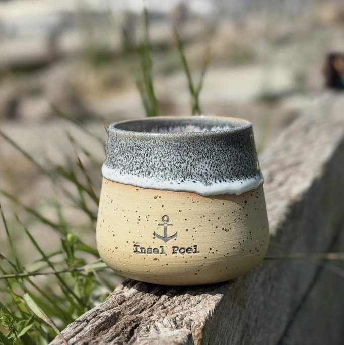 Eine handgefertigte Tasse mit grauem Rand und "Beach Post"-Aufdruck auf einem Holzstück.