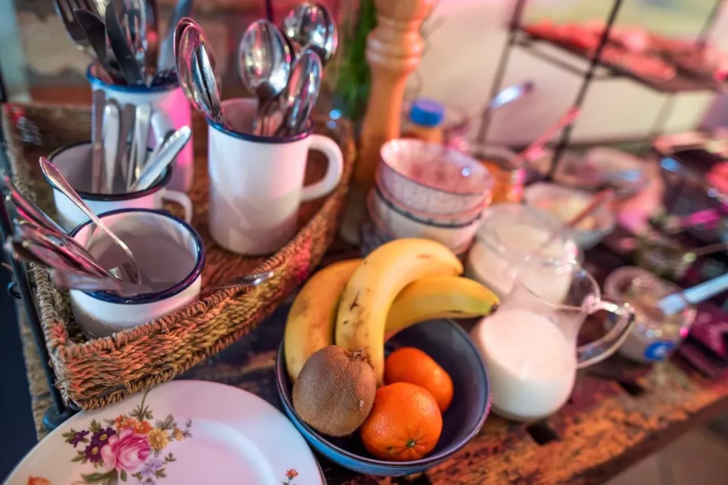 Früchte wie Bananen und Mandarinen in Schalen, umgeben von Besteck und Tellern.