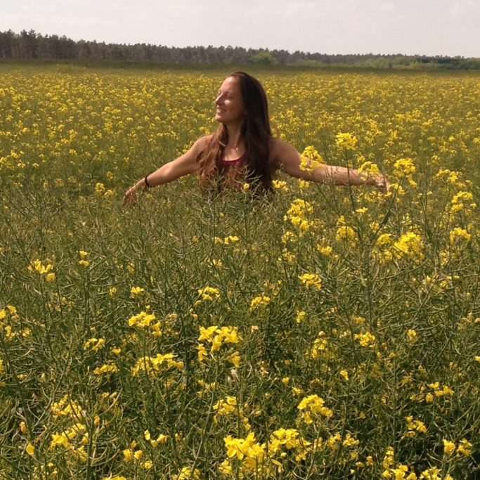Frau mit outgestreckten Armen in einem blühenden Feld voller gelber Blumen.