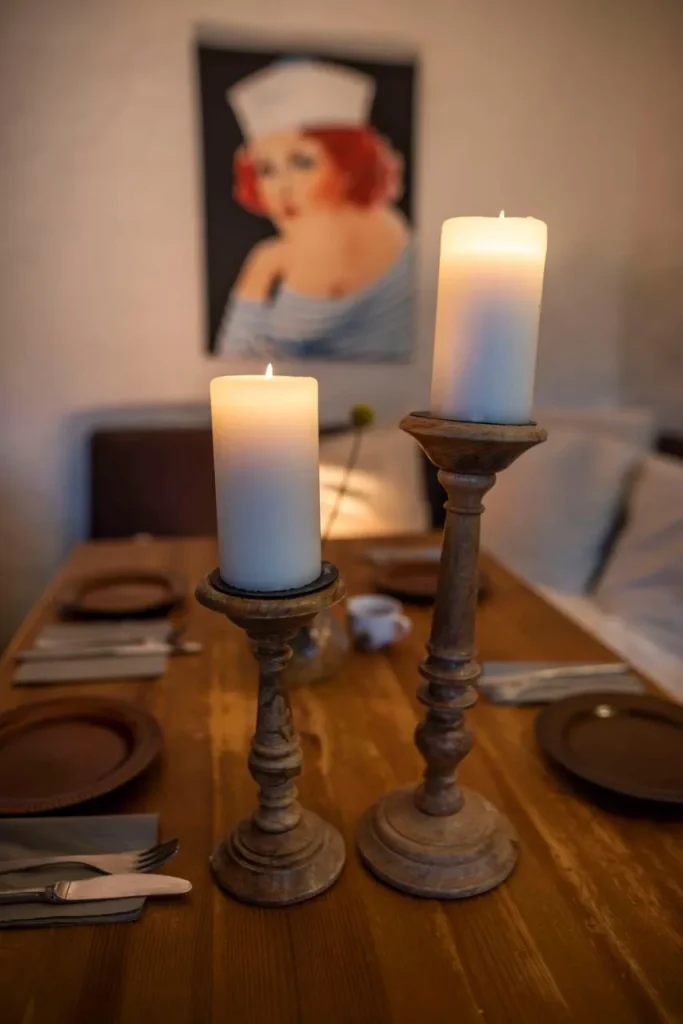 Zwei Kerzenleuchter mit Kerzen auf einem rustikalen Tisch, Hintergrund mit einem Bild.